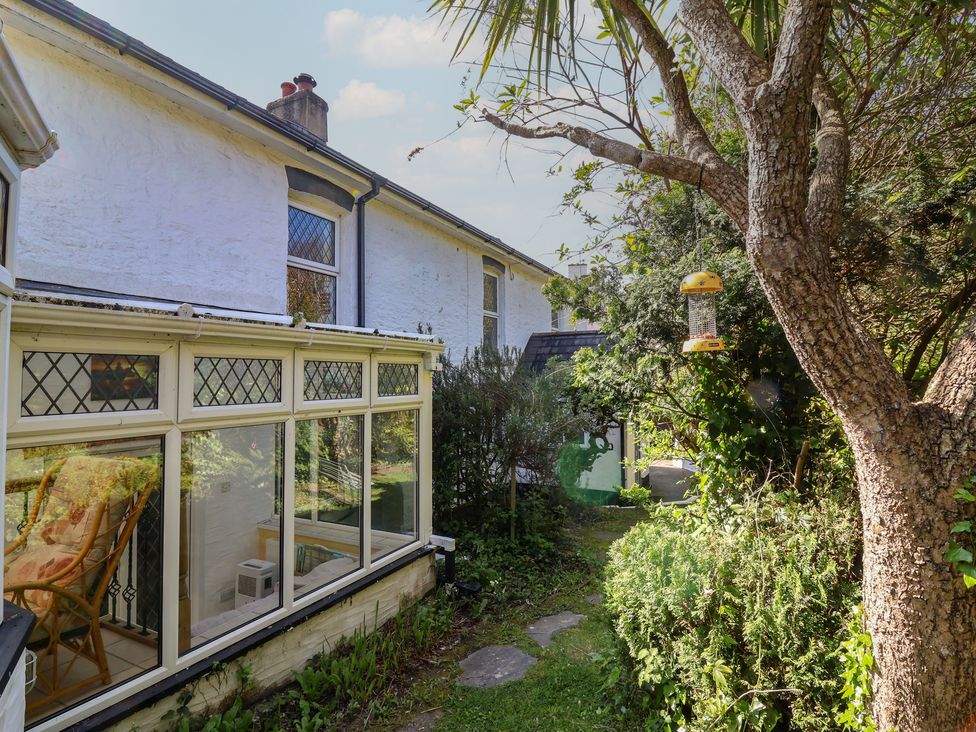 A garden with a conservatory and bird feeder at Honey Cottage in Ilfracombe