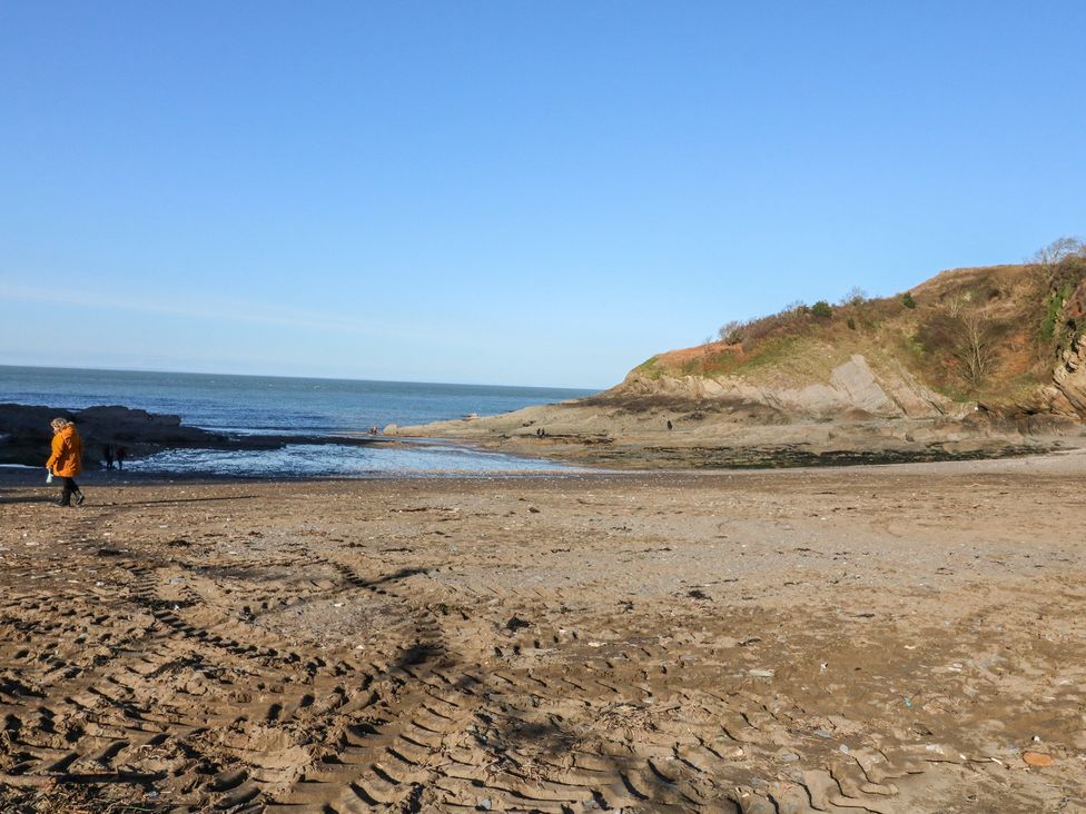 A beach with a person walking near the shore at Honey Cottage in Ilfracombe