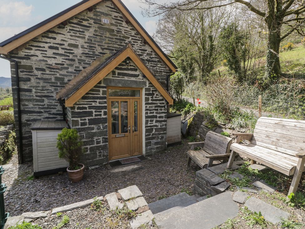 An outdoor area with a stone building and wooden seating at Ysgoldy in Dolwyddelan