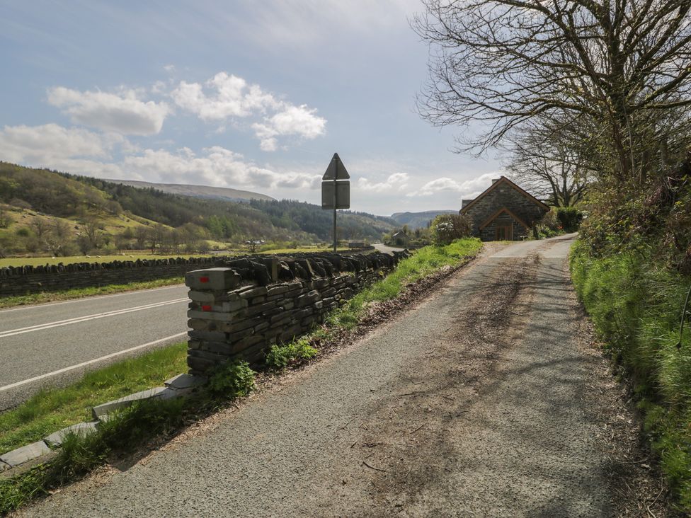 A road with a stone wall and a house at Ysgoldy in Dolwyddelan