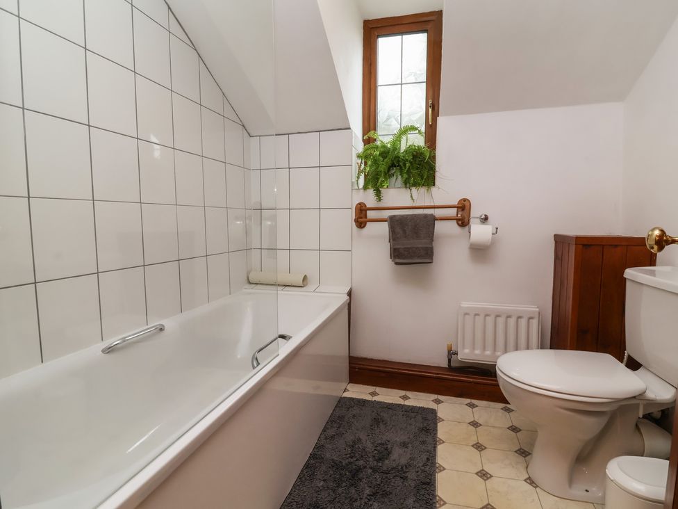A bathroom with a bathtub, toilet, and window at Denhill Cottage