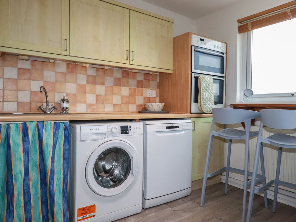 A kitchen featuring a washing machine, a dishwasher, and an oven at 38 Surf View in Newquay