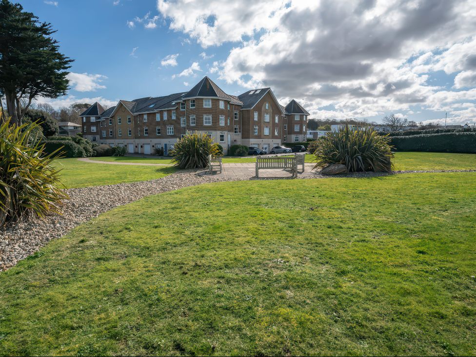 An outdoor area with a building, grass, a pathway, and a bench at 17 Solent Landing in Bembridge