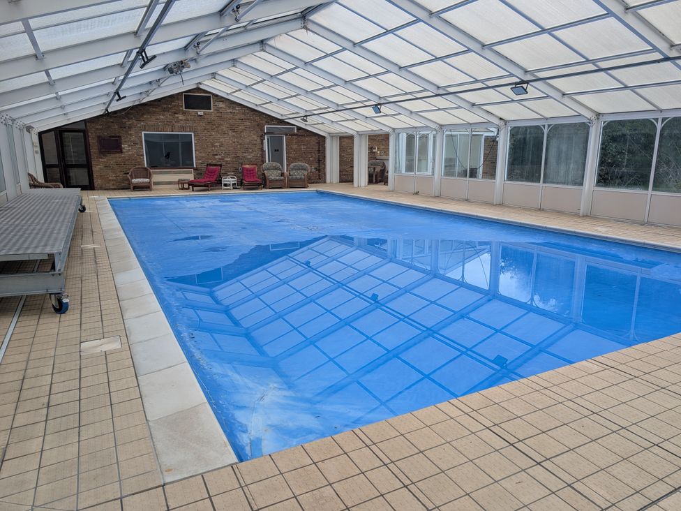 An indoor swimming pool area with seating and tiled flooring at Heath Lodge Iver