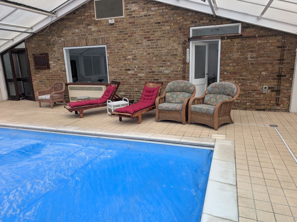 An indoor pool area with loungers and woven chairs at Heath Lodge Iver