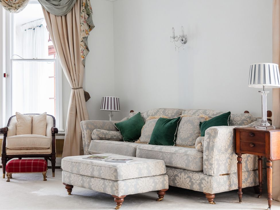 A living room with a sofa, armchair, ottoman, and side table at Violet House in Iver