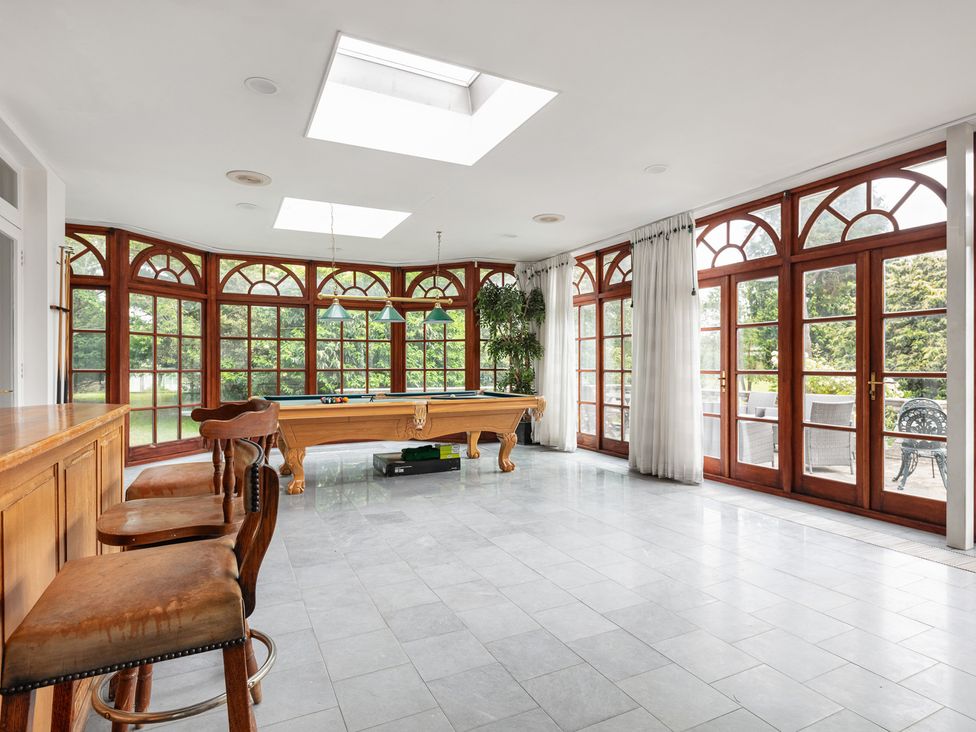 A conservatory with a pool table and large windows at Violet House in Iver