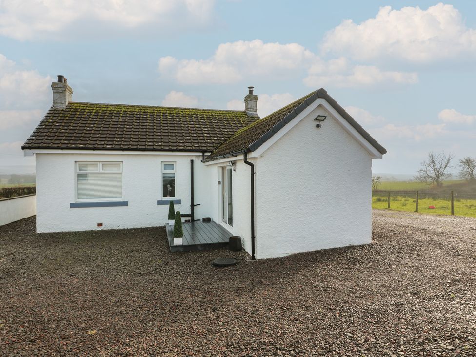 A white house with a deck and gravel area at Marchdyke Farm Cottage Dalton near Annan