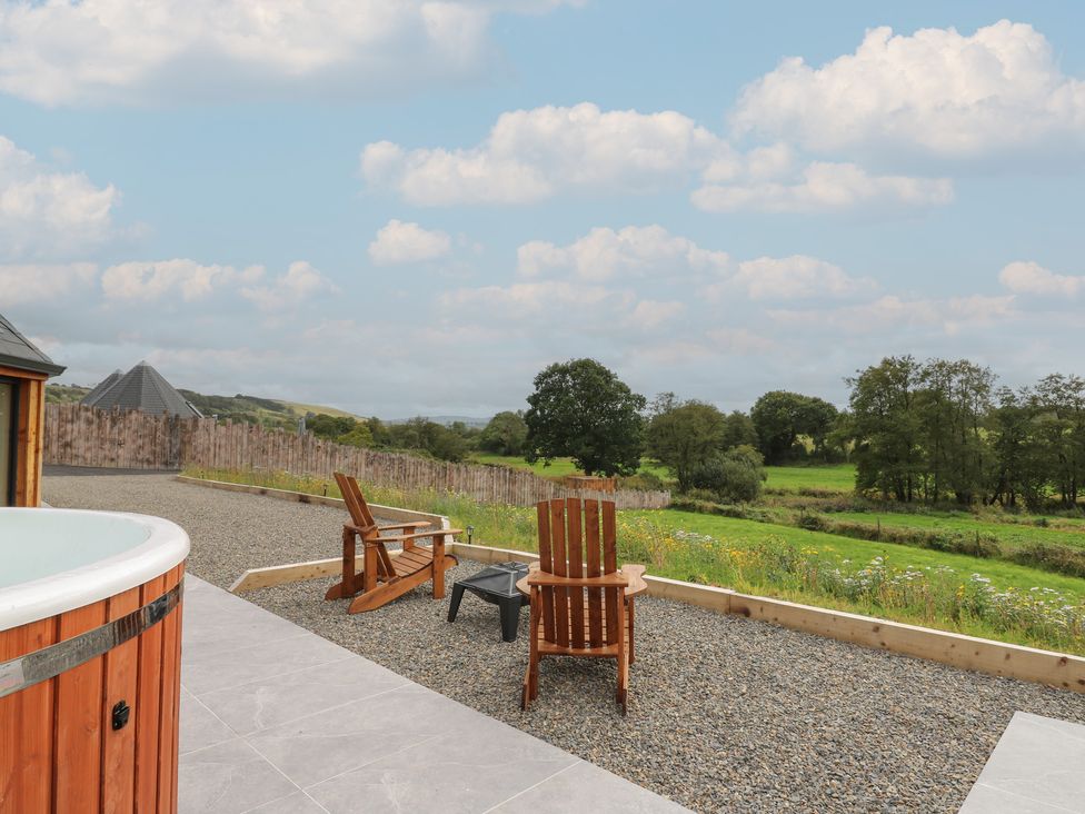 An outdoor area with a hot tub and wooden chairs at Yr Awen in Lampeter