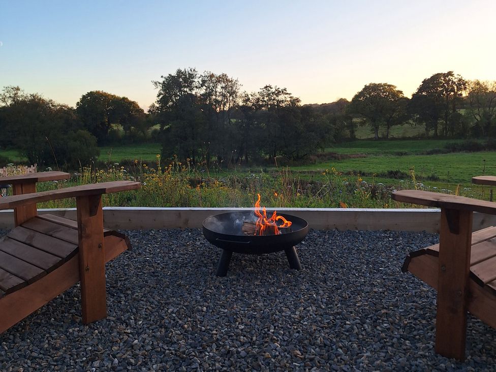 An outdoor area with a fire pit and wooden chairs at Yr Awen Near Lampeter