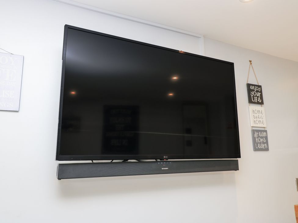 A television mounted on a wall with a soundbar below in The Chill Garden Room Shepton Mallet