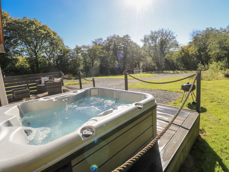 A hot tub on a deck with outdoor seating and a barbecue grill at Dwrgi Llanybydder