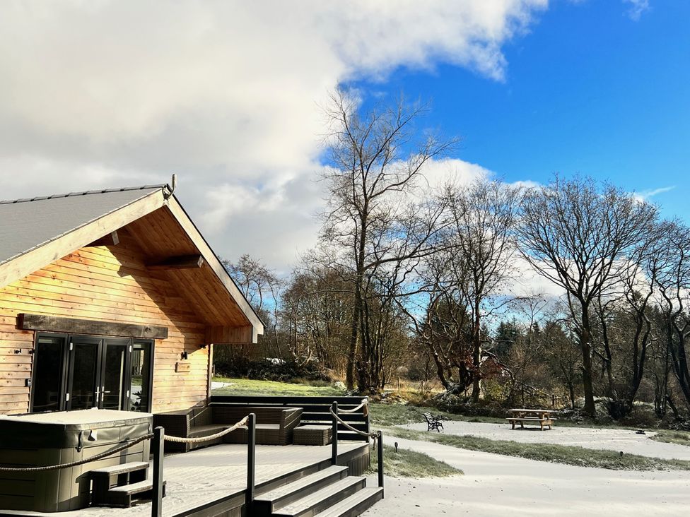 A wooden cabin with a deck and hot tub in a snowy outdoor area at Dwrgi Aber near Llanybydder