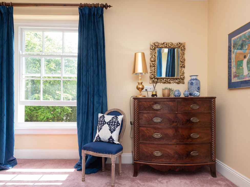 A bedroom with a window, lamp, chest of drawers, chair, and decor at The Old Vicarage in St Issey