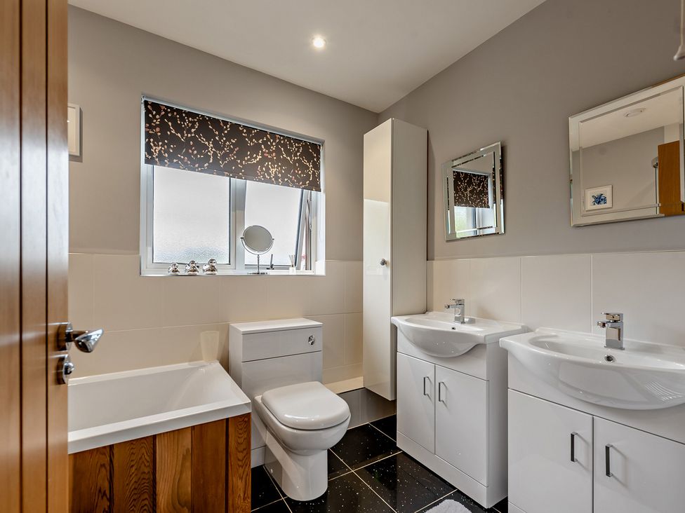 A bathroom with a bath tub and two wash basins at Sea Haze in Tenby