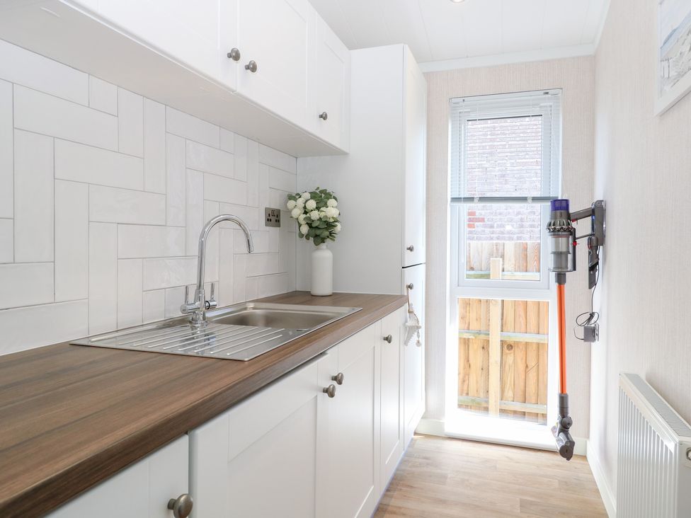 A laundry room with a sink and cabinets at Sandy Snug in Bacton