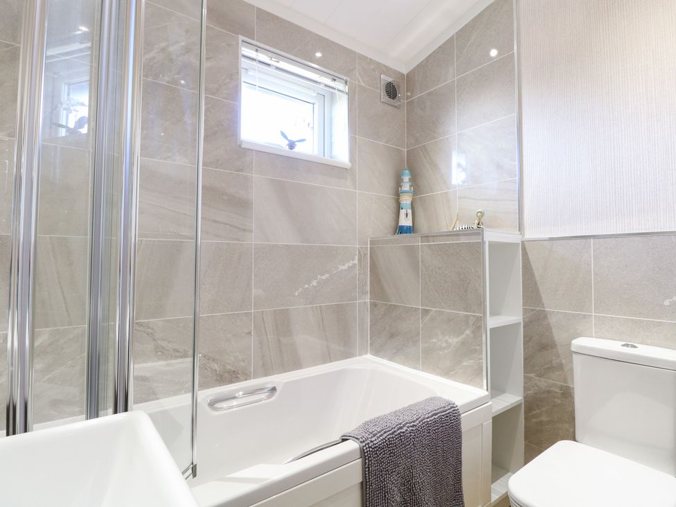 A bathroom with a bath tub, toilet and shower at Sandy Snug in Bacton