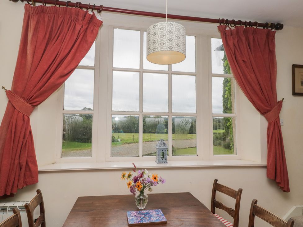 A dining room with a window and a table with flowers at Huntsman's Cottage in Cartmel