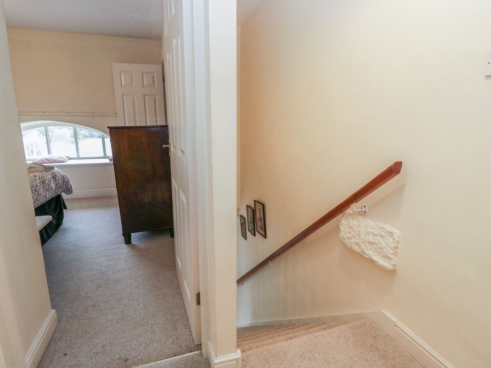 A hallway with a staircase and a view into a bedroom at Huntsman's Cottage in Cartmel