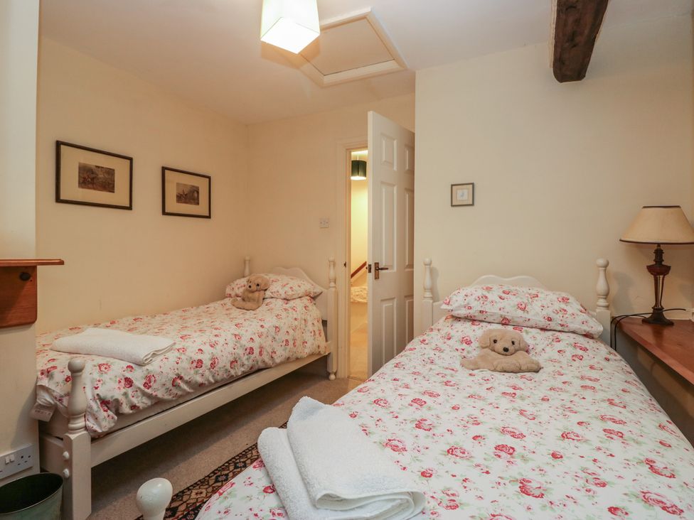 A bedroom with two beds and a teddy bear at Huntsman's Cottage in Cartmel
