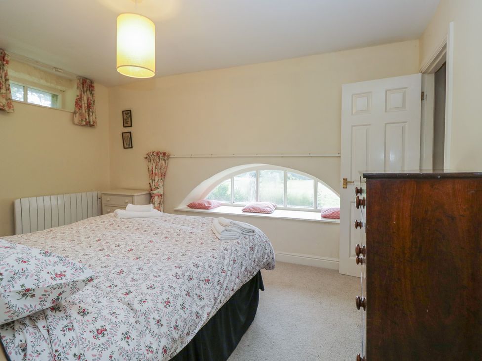 A bedroom with a bed and window at Huntsman's Cottage in Cartmel