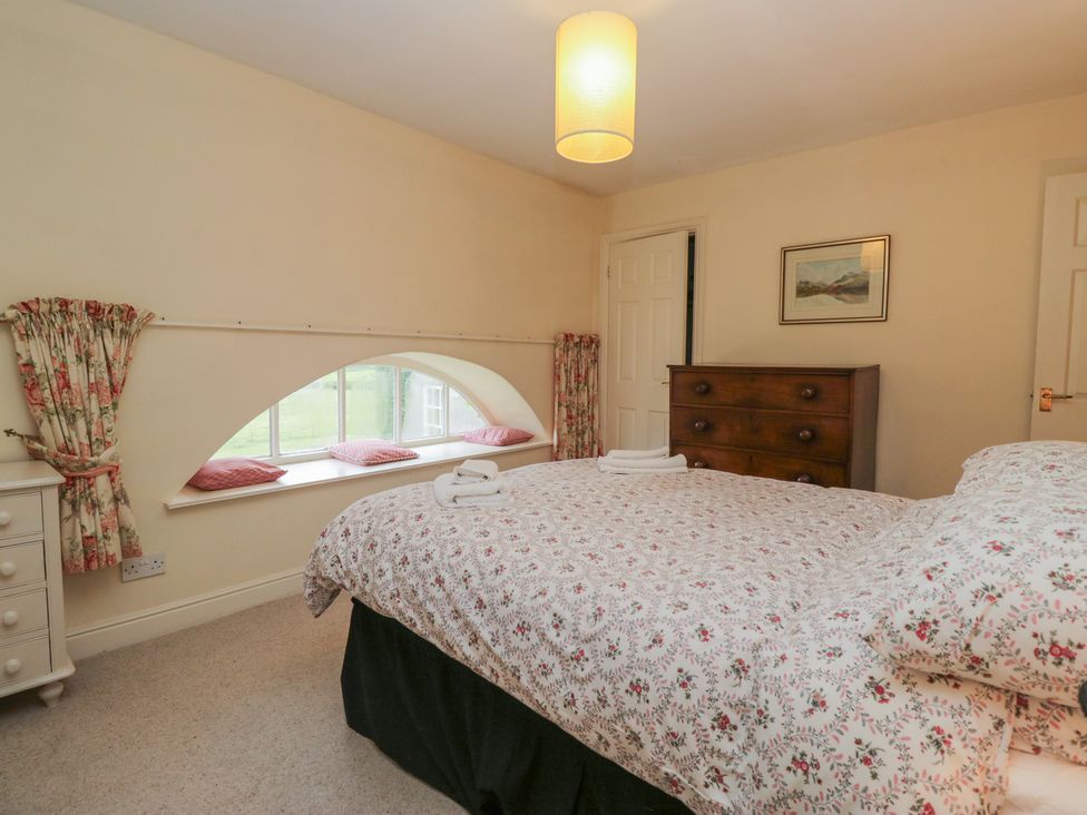 A bedroom with a bed and dresser at Huntsman's Cottage in Cartmel