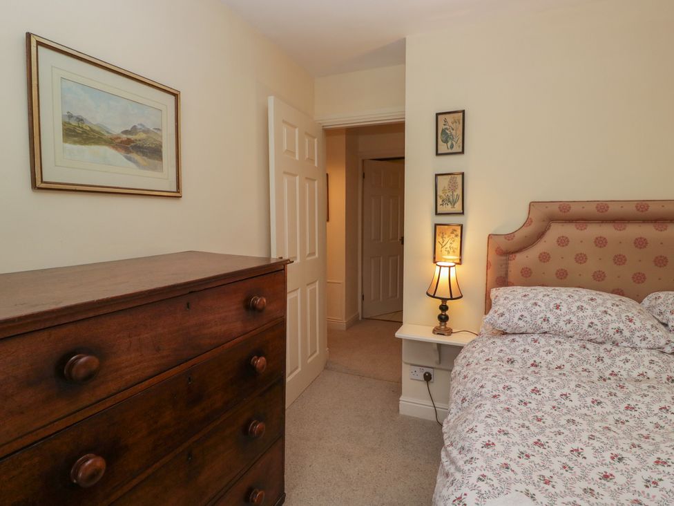 A bedroom with a bed, dresser and lamp at Huntsman's Cottage in Cartmel