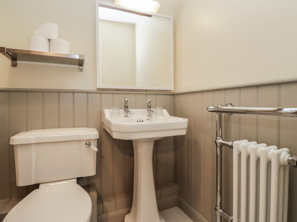 A bathroom with a sink, toilet, and towel rack at Huntsman's Cottage in Cartmel