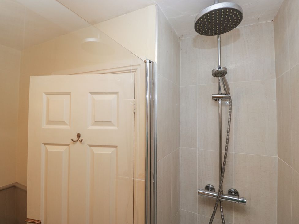 A shower area with a glass panel and a white door at Huntsman's Cottage in Cartmel