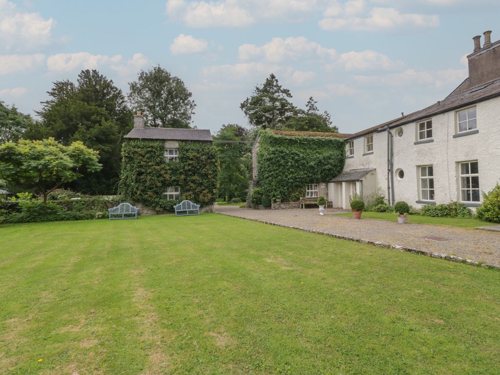 An outdoor area with a lawn, two houses, and benches at Huntsman's Cottage in Cartmel
