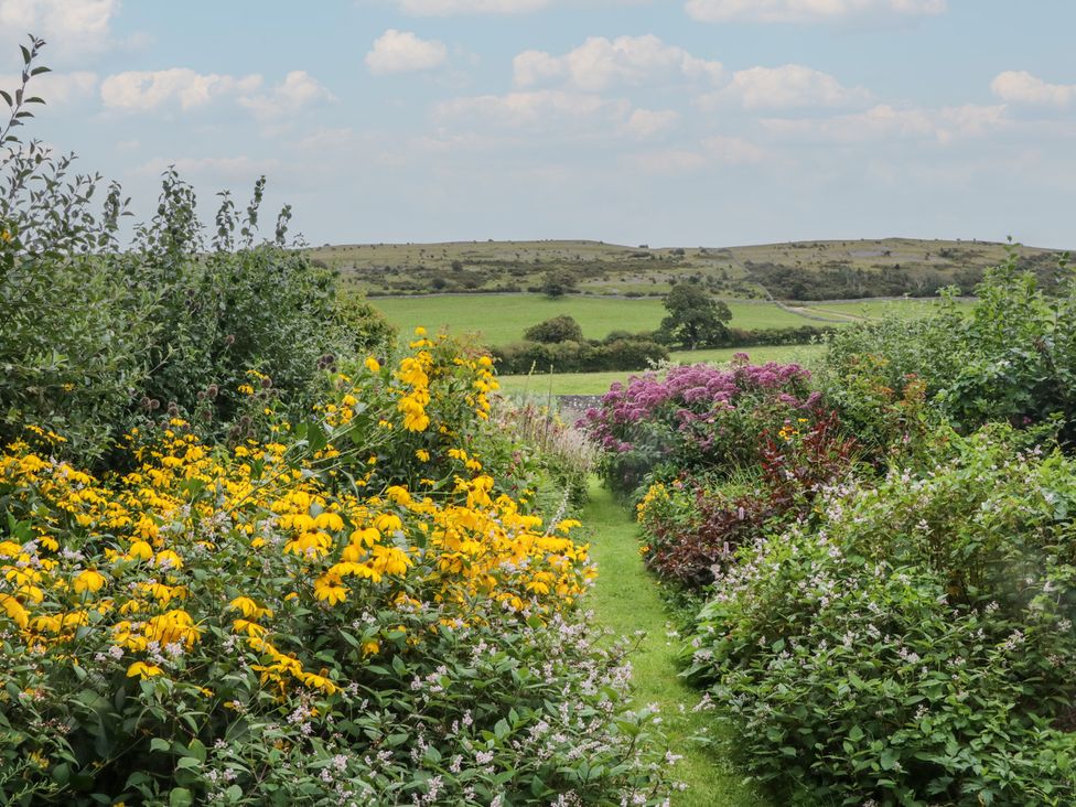 A garden with flowers and greenery leading to hills at The Laundrymaid's Cottage in Cartmel