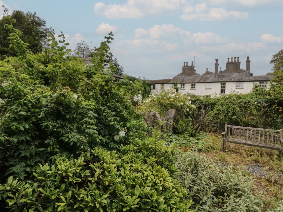 A garden with bushes and a wooden bench at The Laundrymaid's Cottage in Cartmel