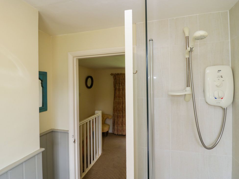 A bathroom with a shower and doorway leading to a staircase at The Laundrymaid's Cottage in Cartmel
