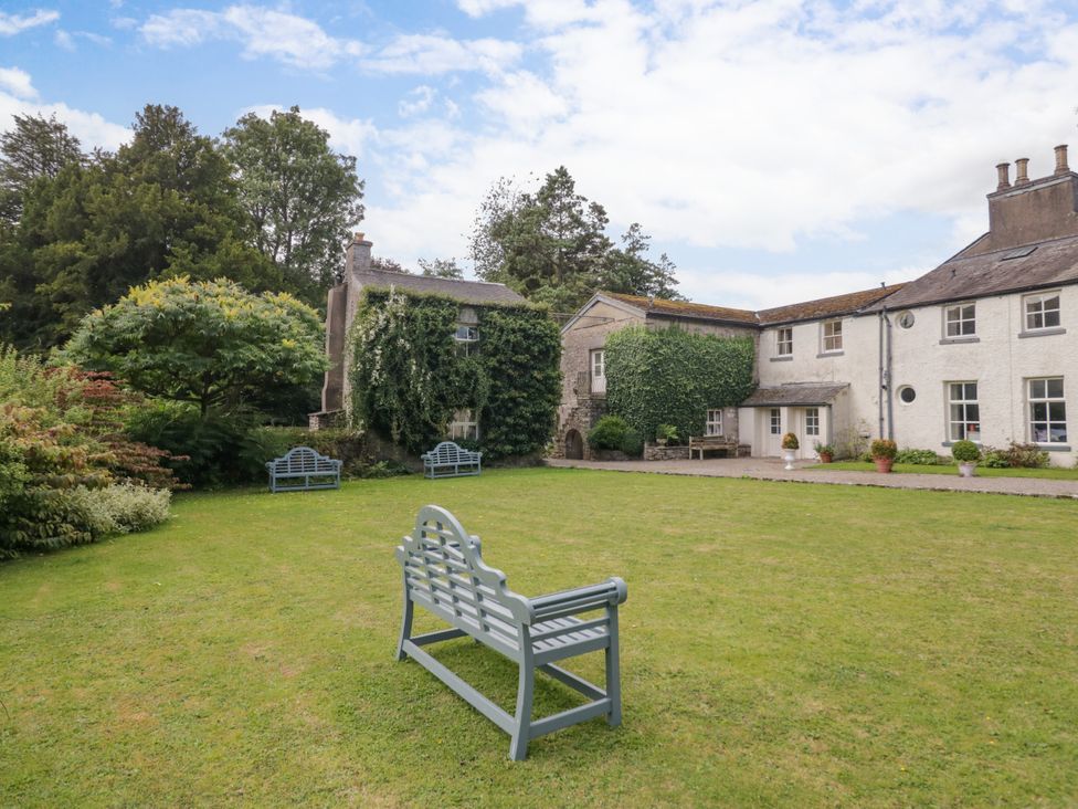 A garden with a view of a building and benches at The Laundrymaid's Cottage in Cartmel
