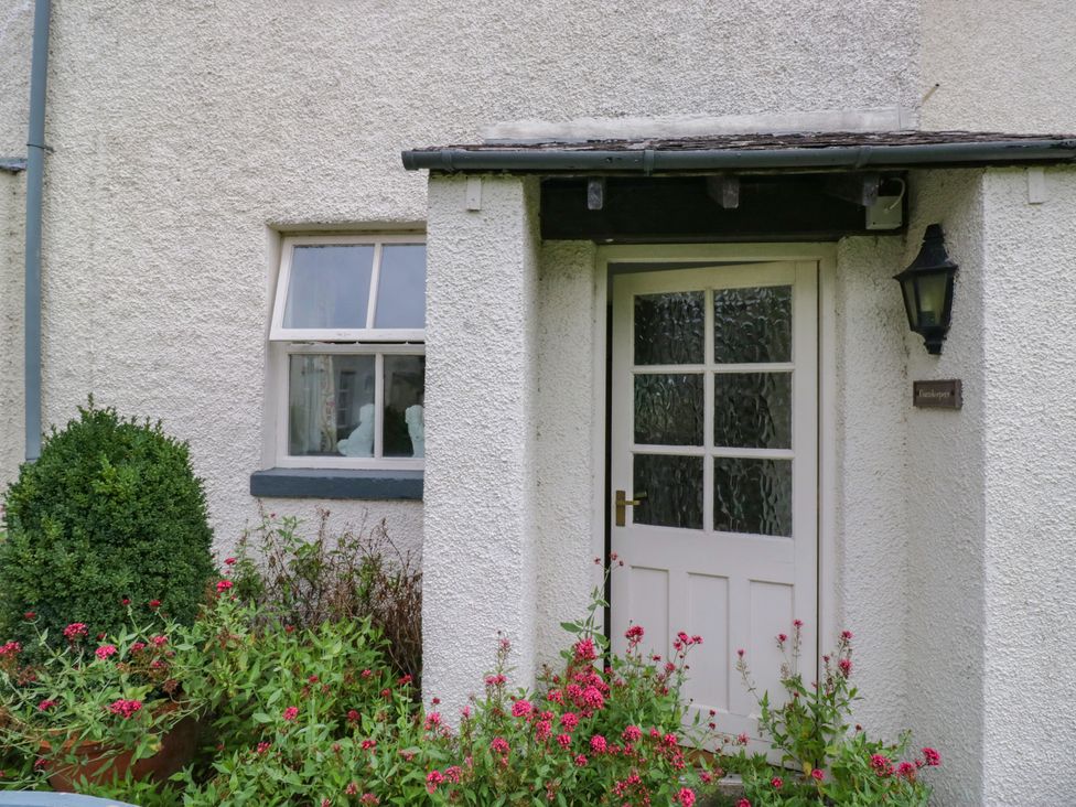 A door with a window next to a plant and flowers at The Gameskeepers Cottage in Cartmel
