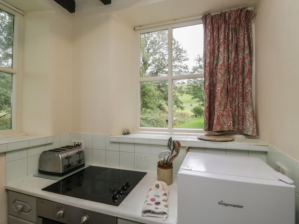 A kitchen with a toaster, cooker, fridge and utensils at The Gameskeepers Cottage in Cartmel