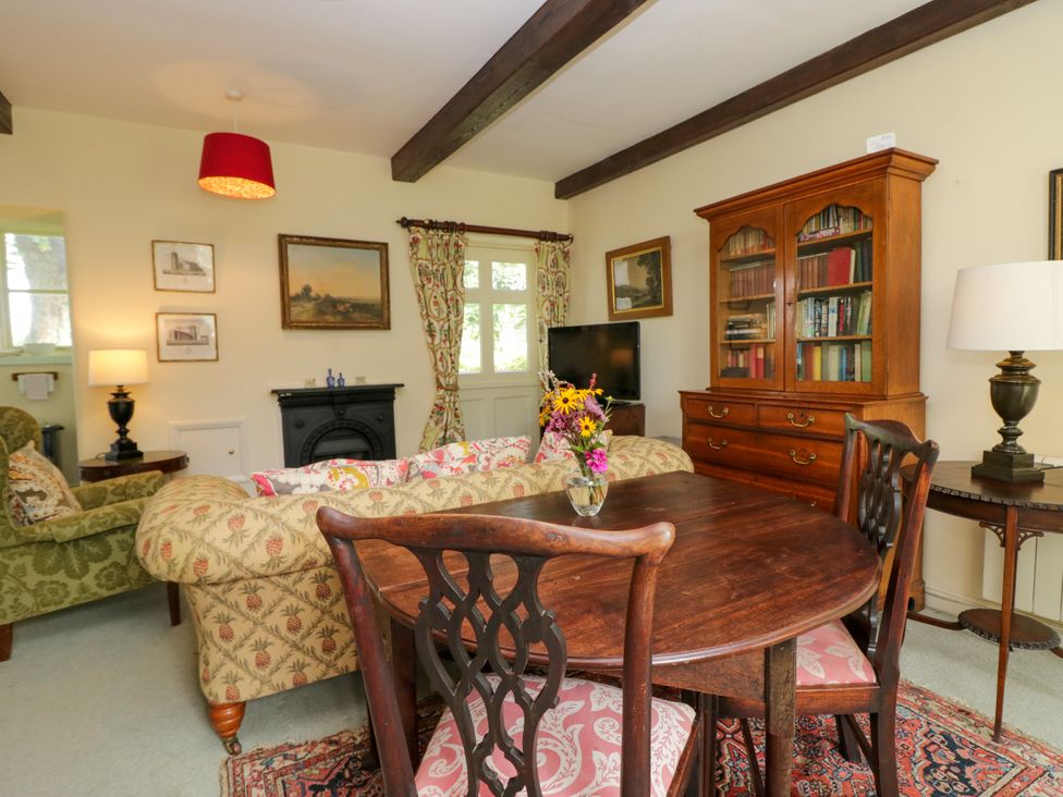 A living room with a dining table and bookshelf at The Gameskeepers Cottage in Cartmel