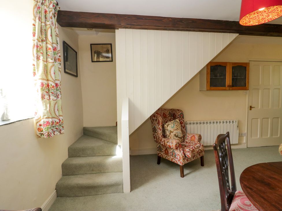 A living room with a staircase and a chair at The Gameskeepers Cottage in Cartmel