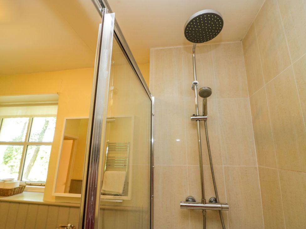 A shower area with a glass door and showerhead at The Gameskeepers Cottage in Cartmel