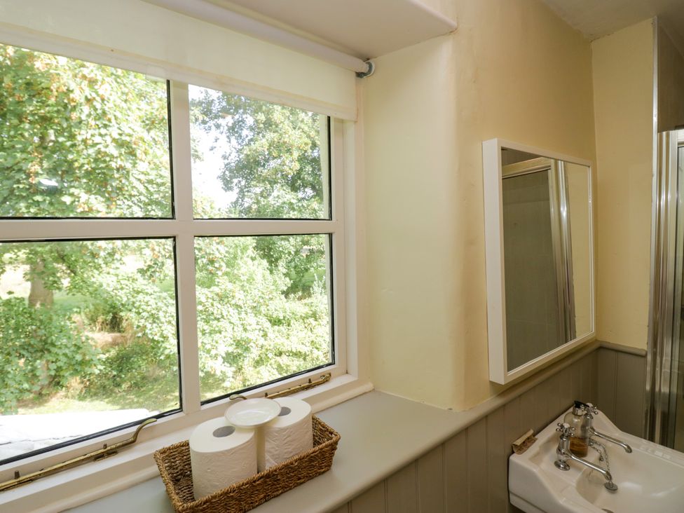 A bathroom with a window, mirror, basin, and shower at The Gameskeepers Cottage in Cartmel