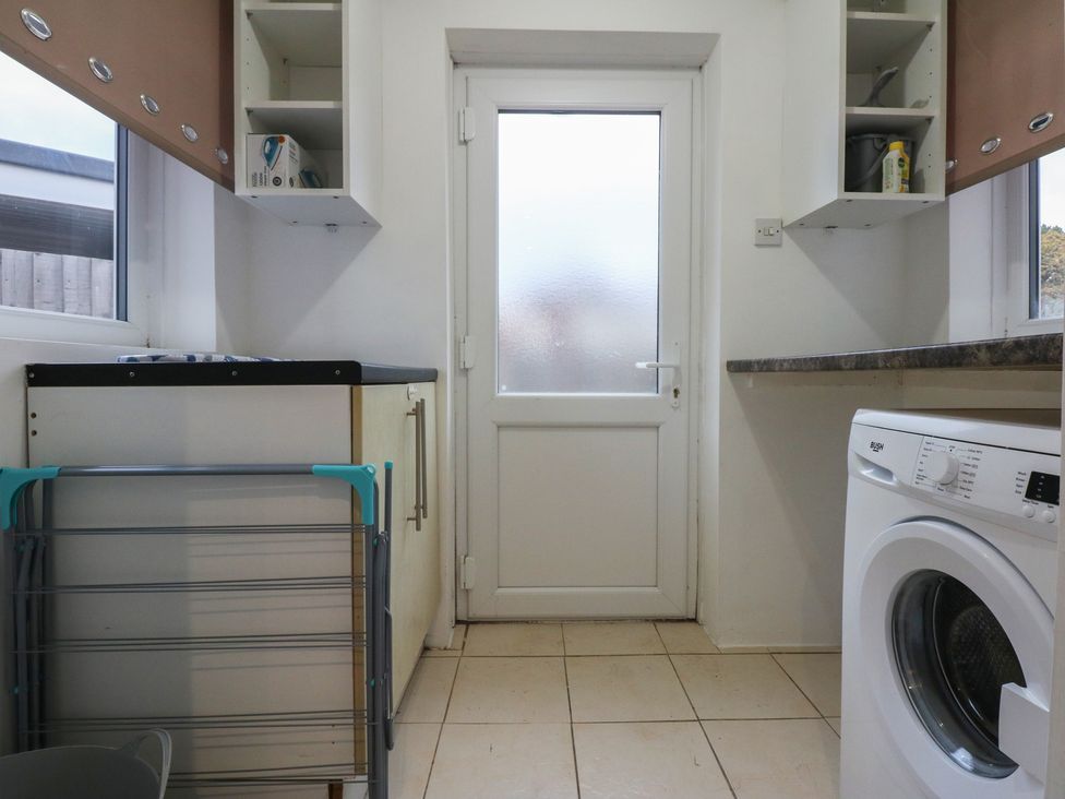 A laundry room with a washing machine and shelves at Tan Y Mynydd Dwygyfylchi