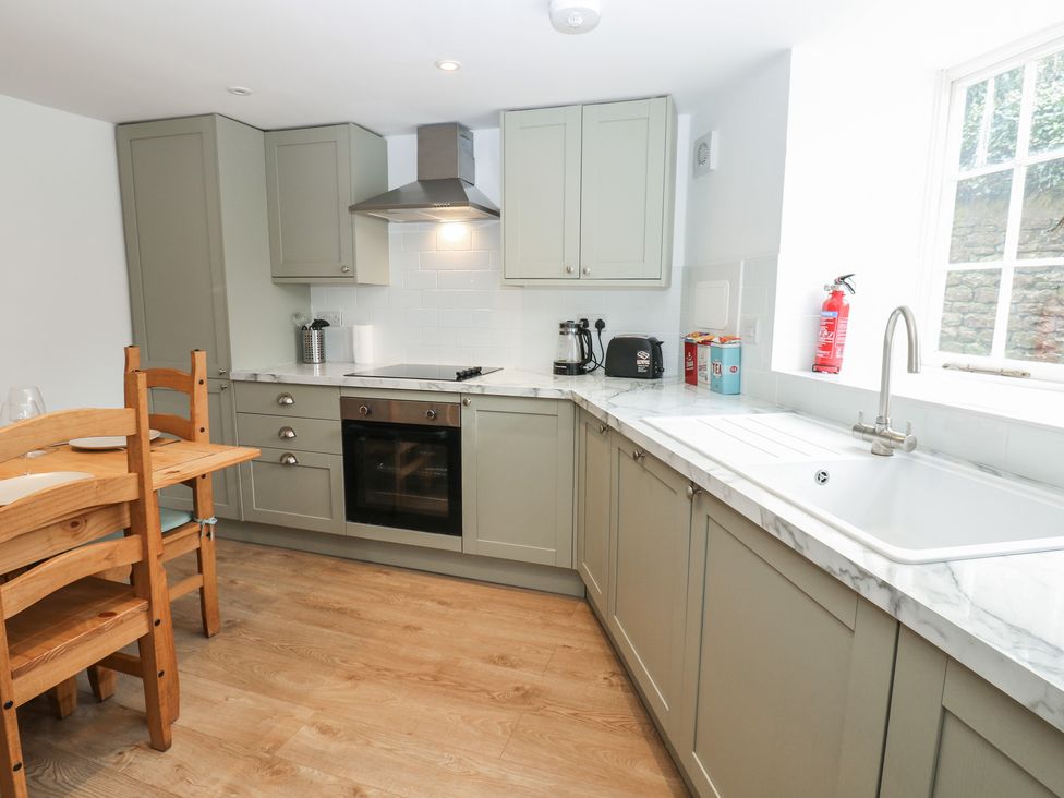 A kitchen with cabinets, counter, oven, sink, table, and chairs at Salvin Cottage in Alston