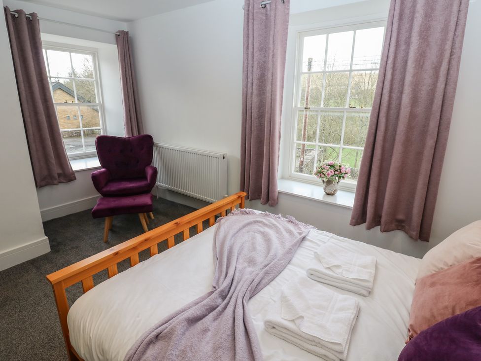 A bedroom with a bed, armchair, and window at Salvin Cottage in Alston
