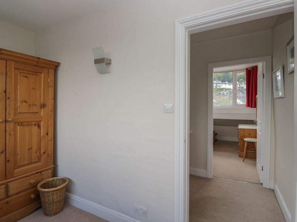 A bedroom with a wardrobe, basket, and doorway to another room at Cloud Cottage Ambleside
