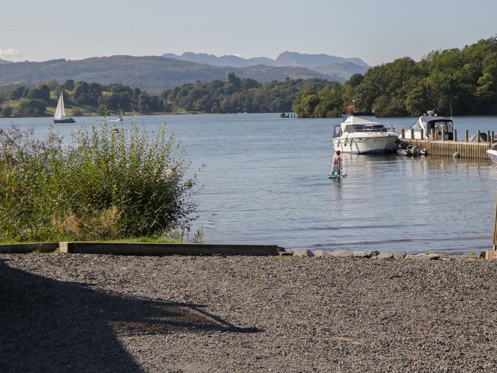 A waterfront scene with boats and a man on a paddleboard at Moon Cottage near White Cross Bay Holiday Park near Troutbeck Bridge