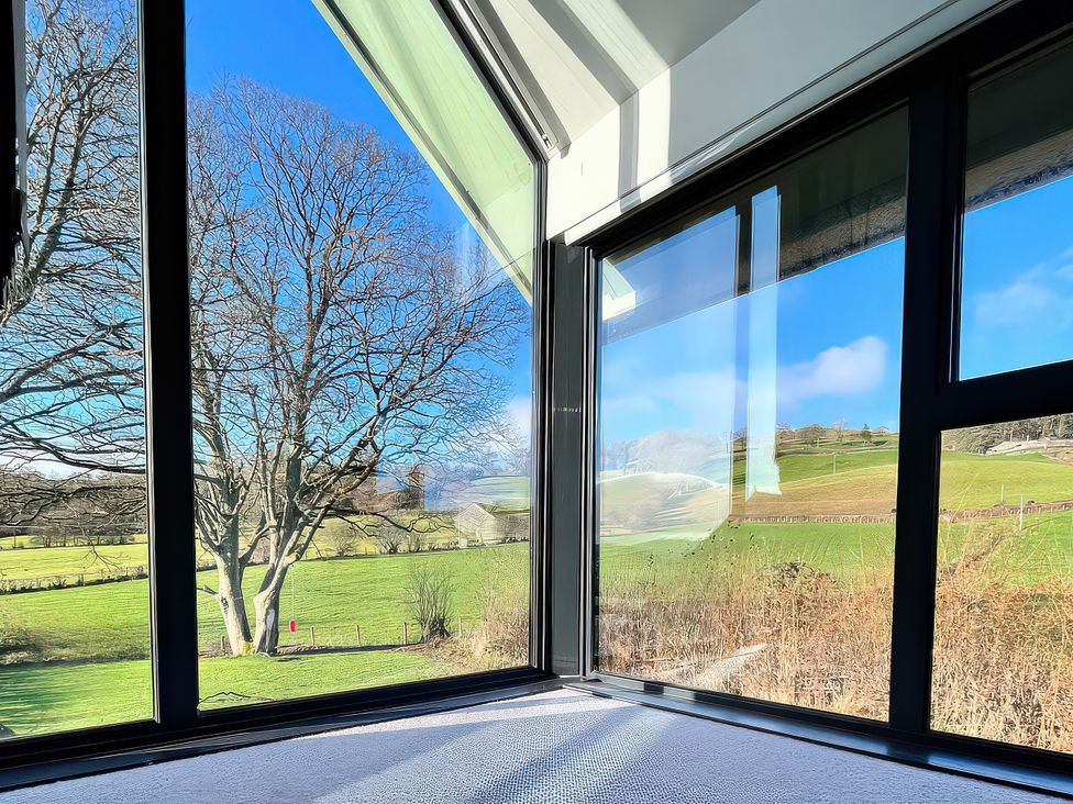 A view of a tree and grass fields through large windows at Hen Stablau Dinmael near Cerrigydrudion