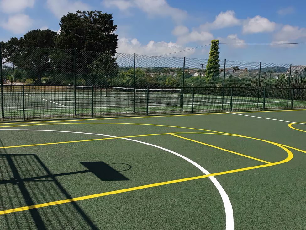 A basketball court with a hoop and adjacent tennis courts at Par Sands Holiday Park - Par