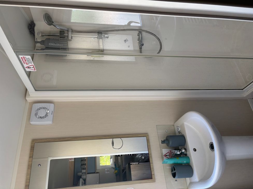A shower and sink with a mirror in a bathroom at an unspecified location