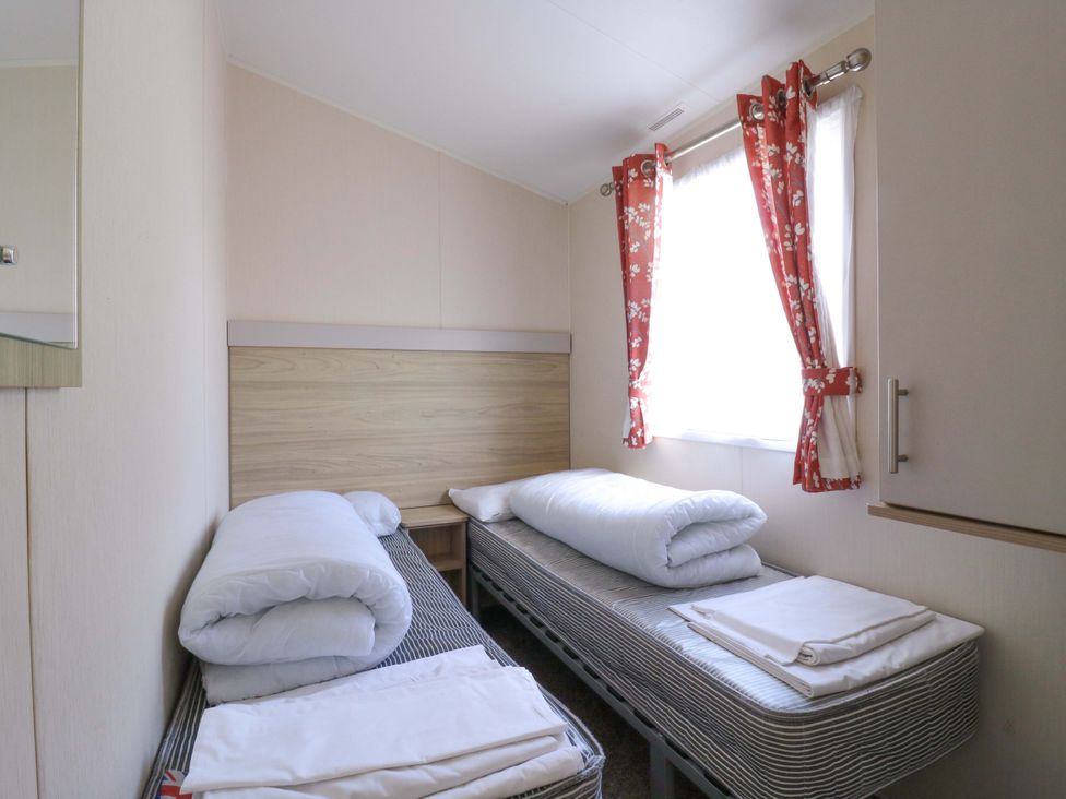 A bedroom with two beds and a window at Singh and Leite Family Caravan St. Osyth