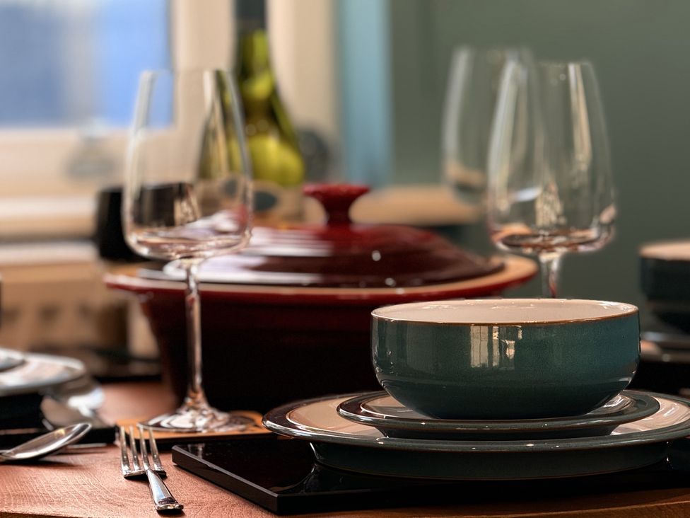 A dining table set with a bowl, plates, glasses, and a casserole dish at Portknockie Cottage, Buckie